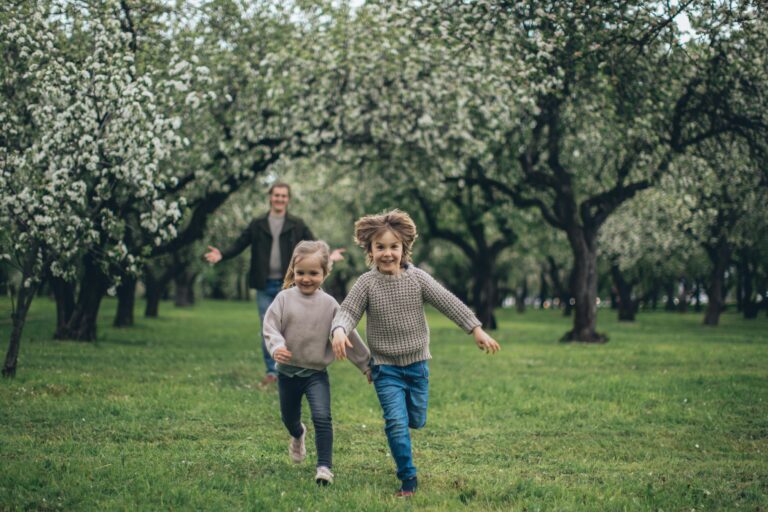A cheerful father and two children running through a blossoming park, enjoying springtime together.