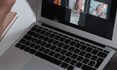 Hands at a laptop showing a group video call in a home office setting.